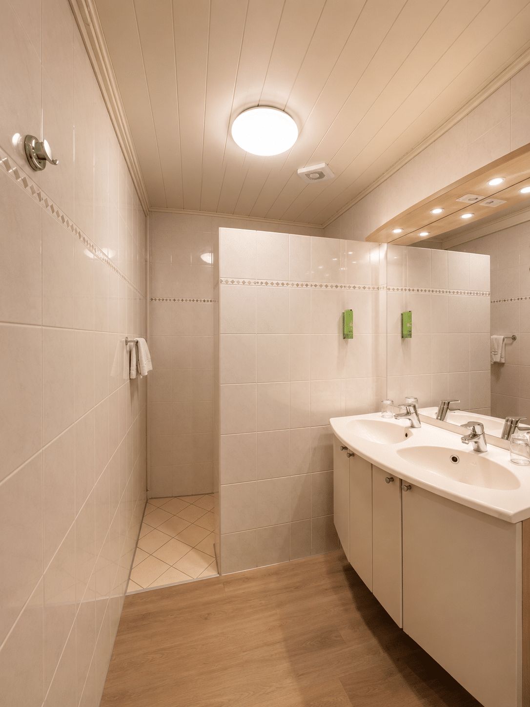 Un baño moderno con ducha a ras de suelo, tocador doble y un espejo grande.
