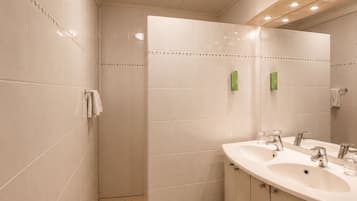 Un baño moderno con ducha a ras de suelo, tocador doble y un espejo grande.