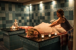 Ein Wellnessbereich mit Massageliege, Statue und Kerzen.