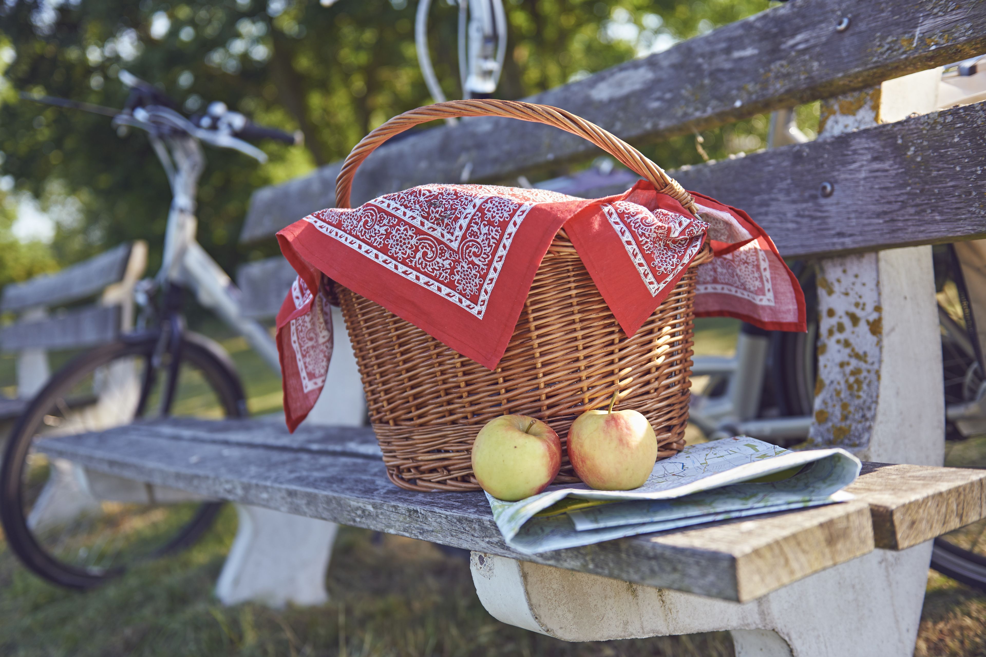 A wicker picnic basket with a red cloth on a bench.