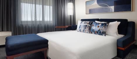 A hotel room with a large bed, a bench, a bedside table, a lamp, and a painting on the wall.