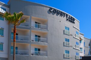 A Courtyard by Marriott hotel with balconies, a palm tree, and a clear blue sky.
