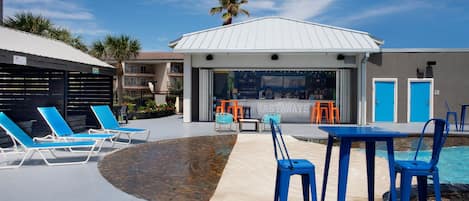 Un área junto a la piscina con sillones de descanso, un bar y una piscina.