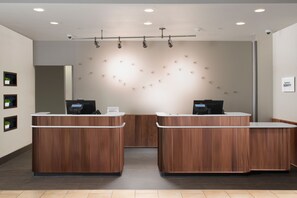 A reception area with two wooden reception desks, a wall-mounted light fixture, and a sign indicating the hotel name. - Courtyard by Marriott Galveston Island (Galveston)