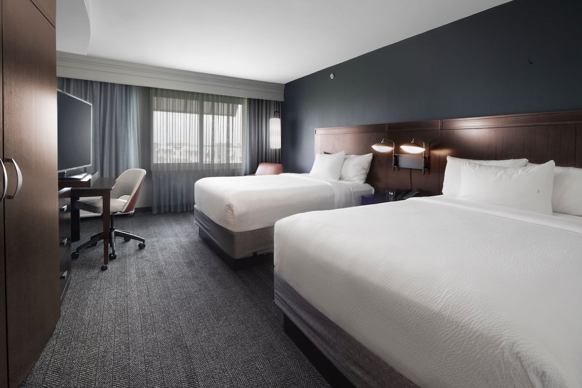 A hotel room with two beds, a desk, a chair, and a television.