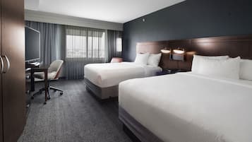 A hotel room with two beds, a desk, a chair, and a television.