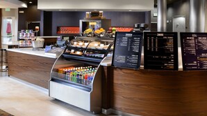 Zona de recepción de hotel con mostrador, dispensador de bebidas y cartel de menú.