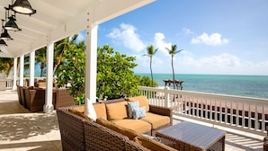 A covered outdoor seating area with wicker furniture, a view of the ocean, and a white railing.