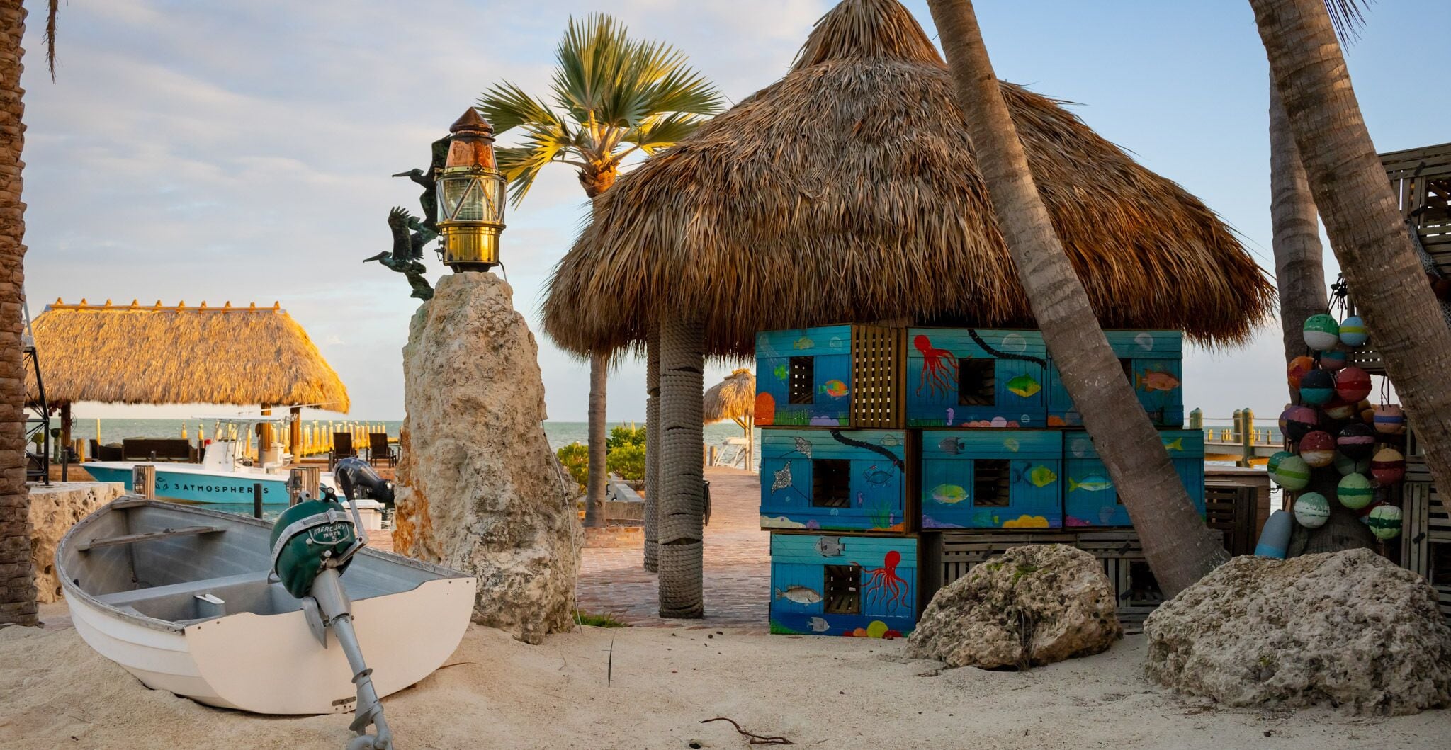 Een strandscène met een rieten hut, een boot en kleurrijke visvormige containers.