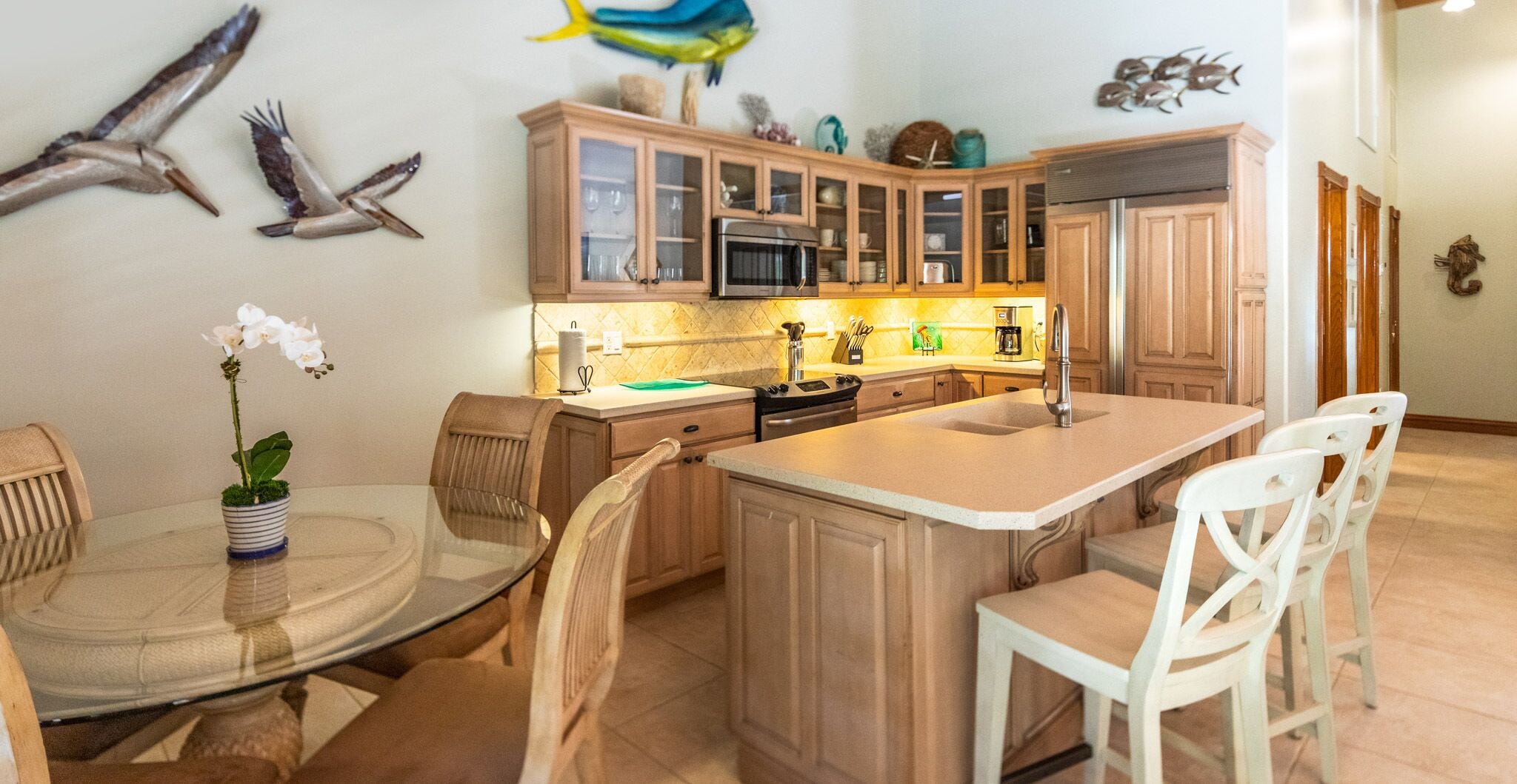 A kitchen with wooden cabinets, a central island with a sink, and a dining area with chairs and a table.