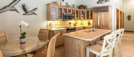 A kitchen with wooden cabinets, a central island with a sink, and a dining area with chairs and a table.