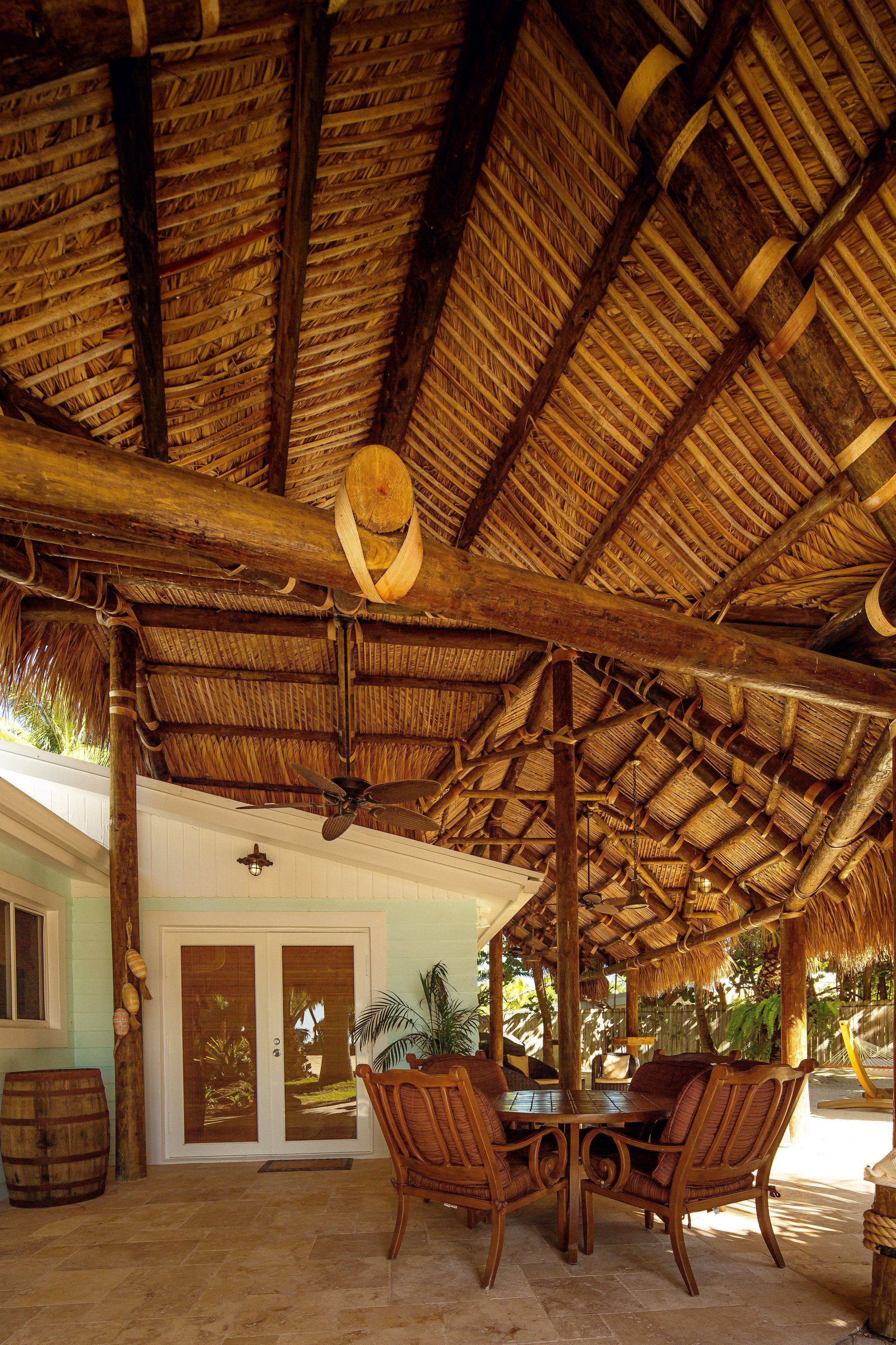 A covered outdoor area with a thatched roof, wooden furniture, and a door leading to a building.