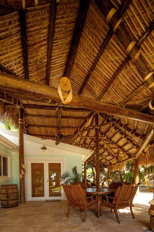 A covered outdoor area with a thatched roof, wooden furniture, and a door leading to a building. - The Caribbean Resort (Islamorada)