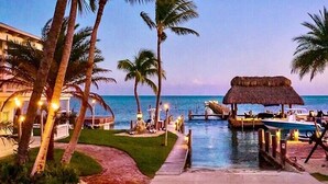 A resort with a pool, palm trees, and a dock with boats.