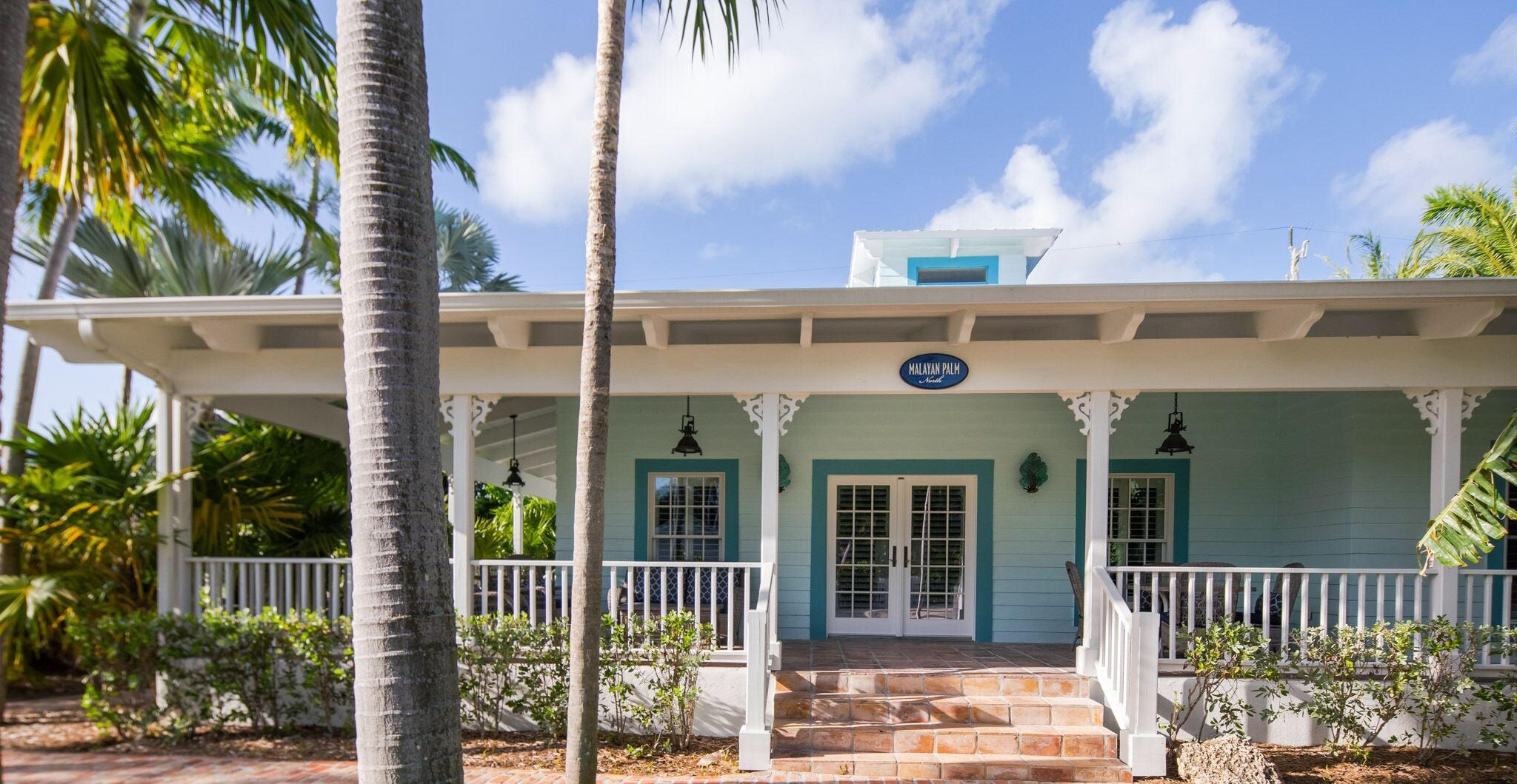 A two-story building with a porch, a sign reading "Malayan Palm," and a clear blue sky.