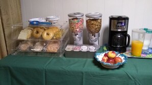 A breakfast setup with a coffee maker, juice, and a bowl of fruit on a table. - Green Valley Motel (Williamstown)