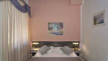 Un dormitorio con cama, dos mesitas de noche, una mesita auxiliar, un cuadro en la pared y una ventana con cortinas.