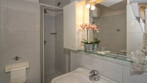 Un baño con cabina de ducha de vidrio, un lavamanos con espejo y una planta en maceta sobre el borde del lavamanos.