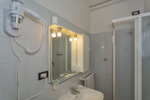 Un bagno dotato di asciugacapelli, specchio, lavandino e doccia.