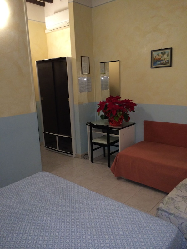 A hotel room with two beds, a small table with a red flower vase, a mirror, and a door leading to a closet. - Hotel Amalfitana (Pisa)