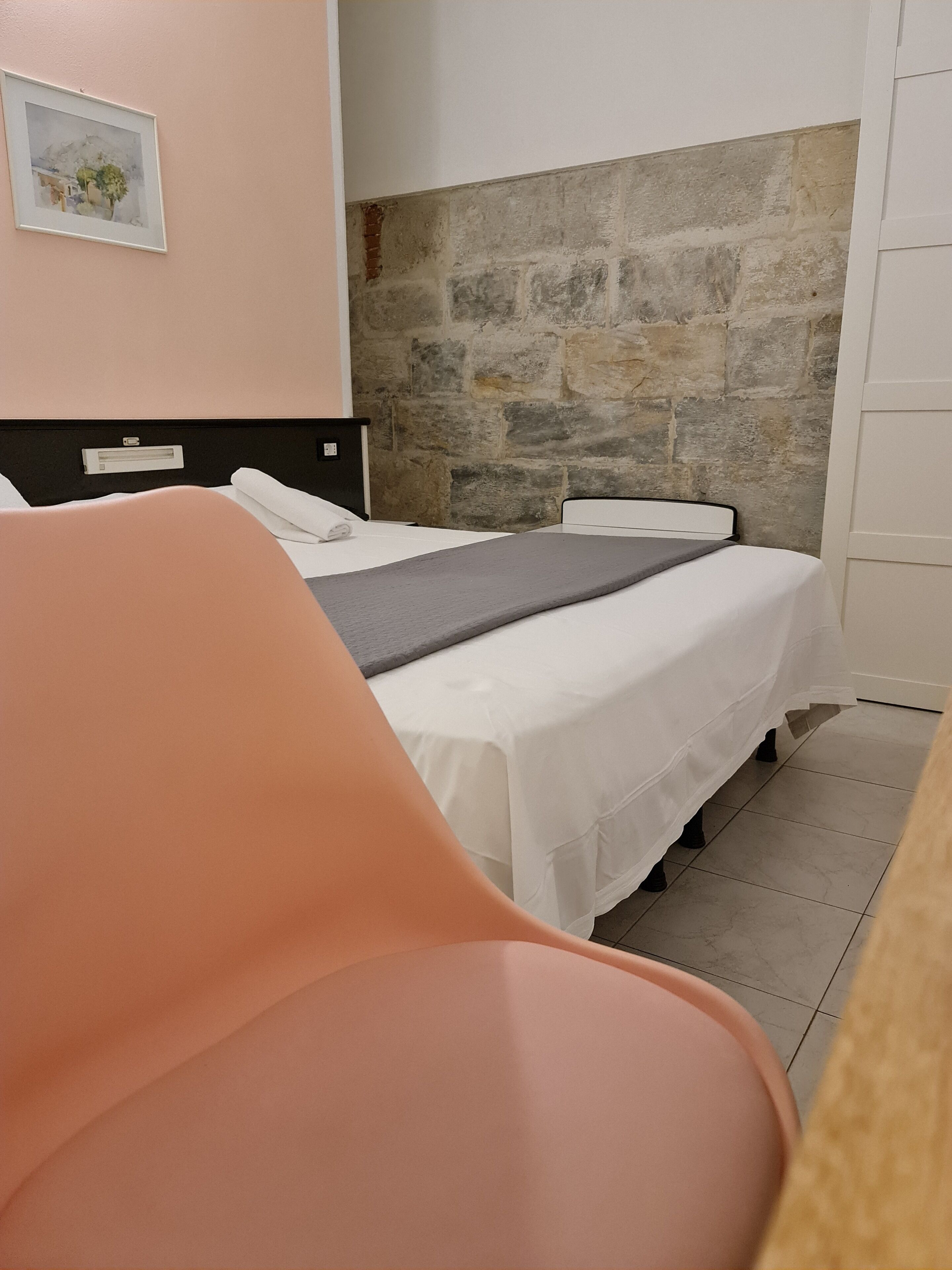 Quarto com uma cama, uma cadeira, uma parede de pedra e um quadro na parede.