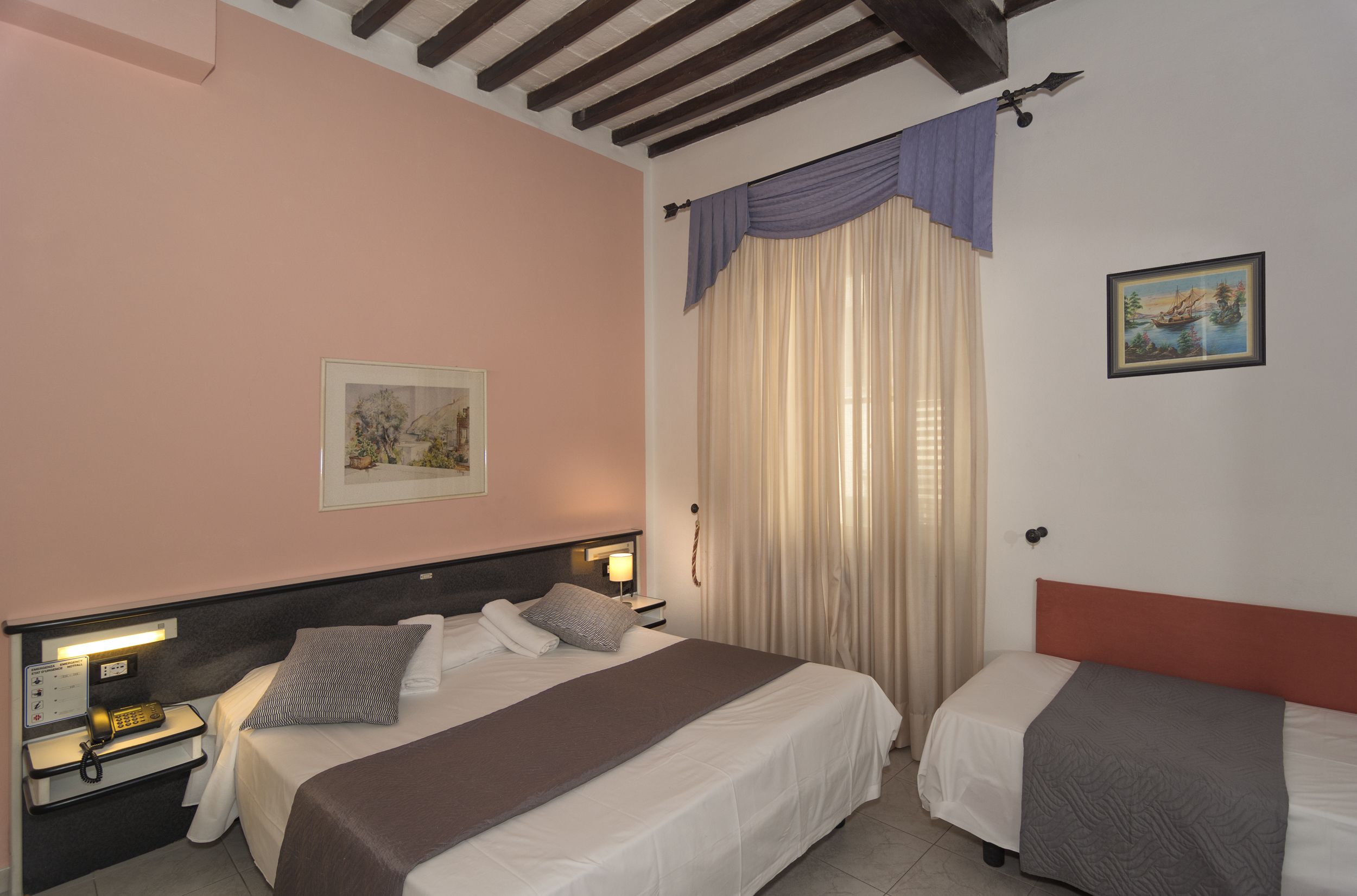 Habitación de hotel con cama, mesitas de noche, teléfono, un cuadro en la pared y ventana con cortinas.