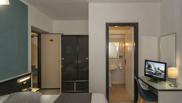 Ein Hotelzimmer mit Bett, Schreibtisch mit Fernseher, Stuhl, Kleiderschrank und einem durch eine geöffnete Tür einsehbaren Badezimmer.