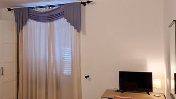 Habitación de hotel con cama, escritorio con televisor, silla y ventana con cortinas.