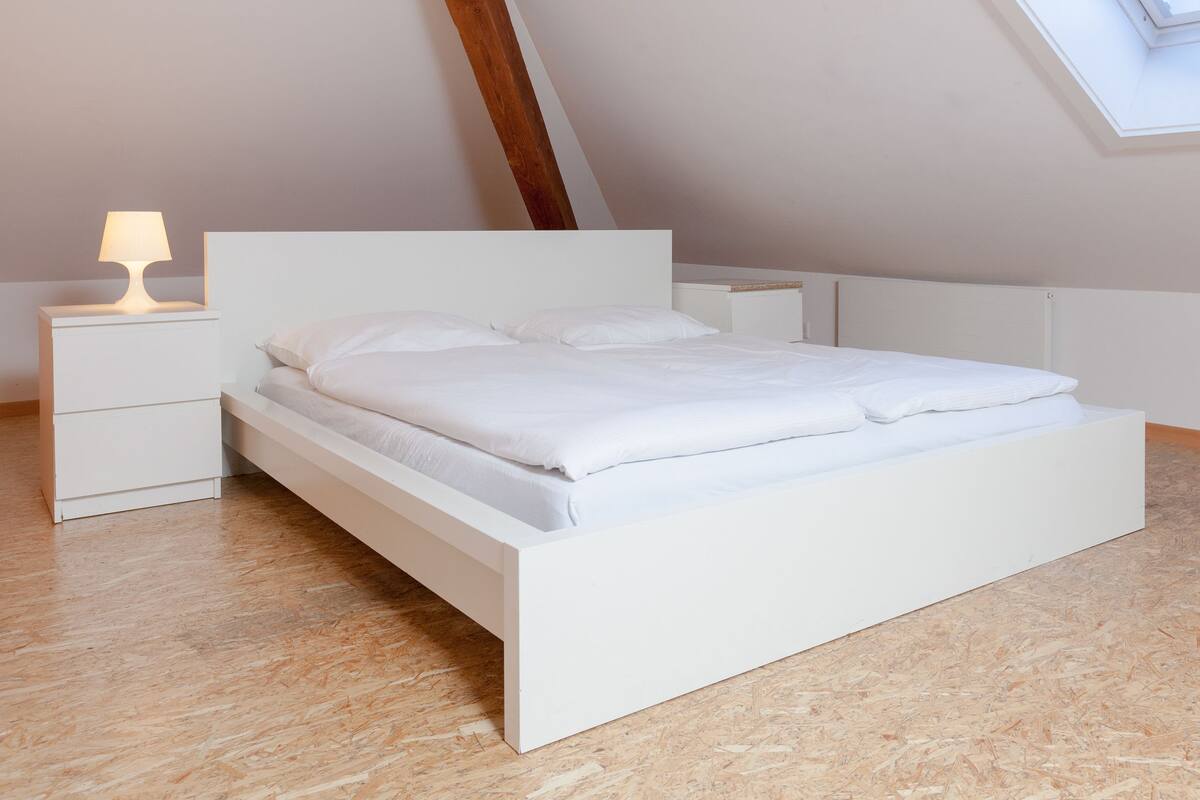 A modern bedroom with a white bed, nightstands, and a skylight.