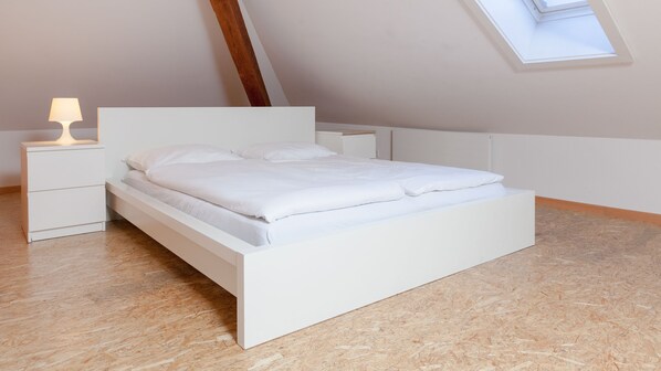 A modern bedroom with a white bed, nightstands, and a skylight.
