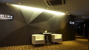 A hotel corridor with a geometric patterned carpet, two white armchairs, a small table with a plant, and directional signs indicating room numbers. - The Art Hotel - Shenzhen (Shenzhen)
