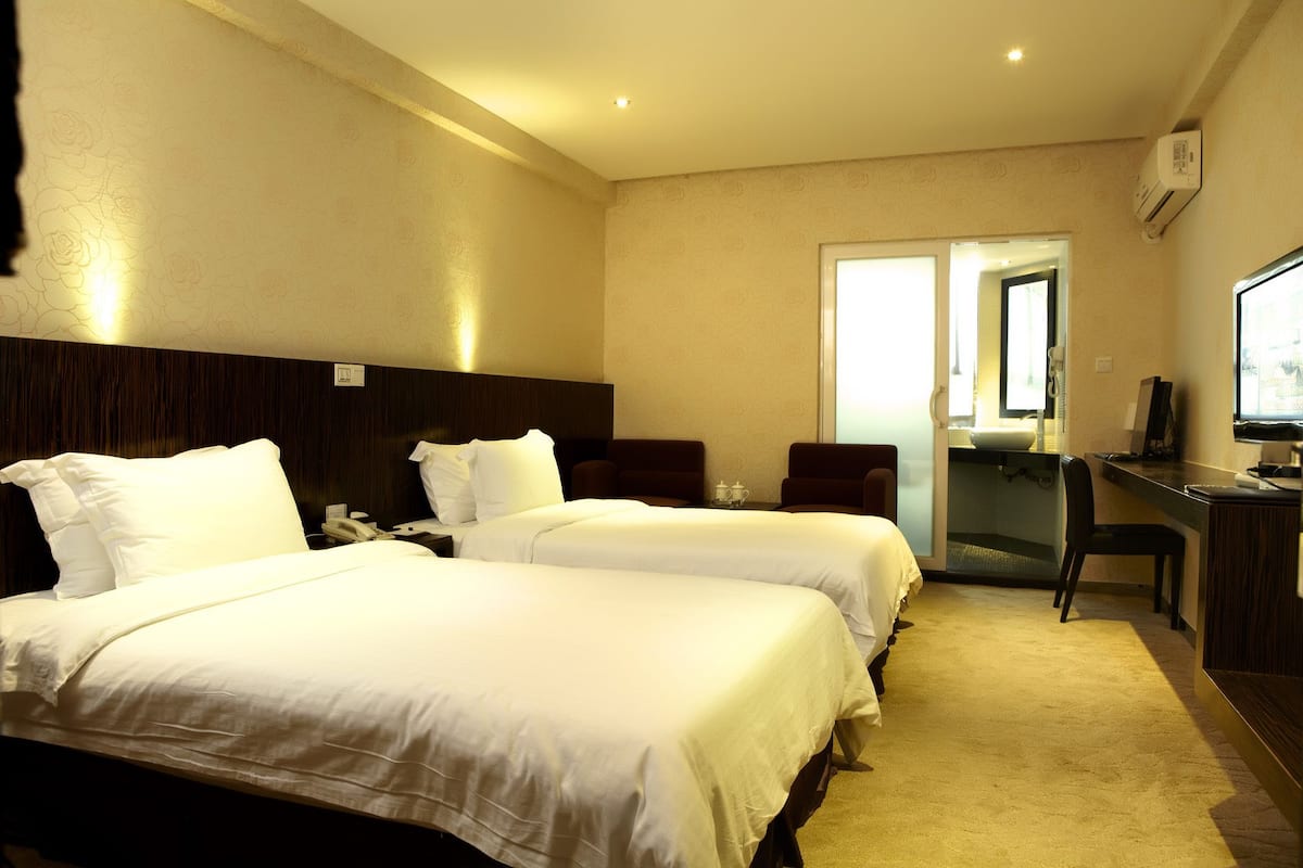 A hotel room with two beds, a desk, a chair, and a television.