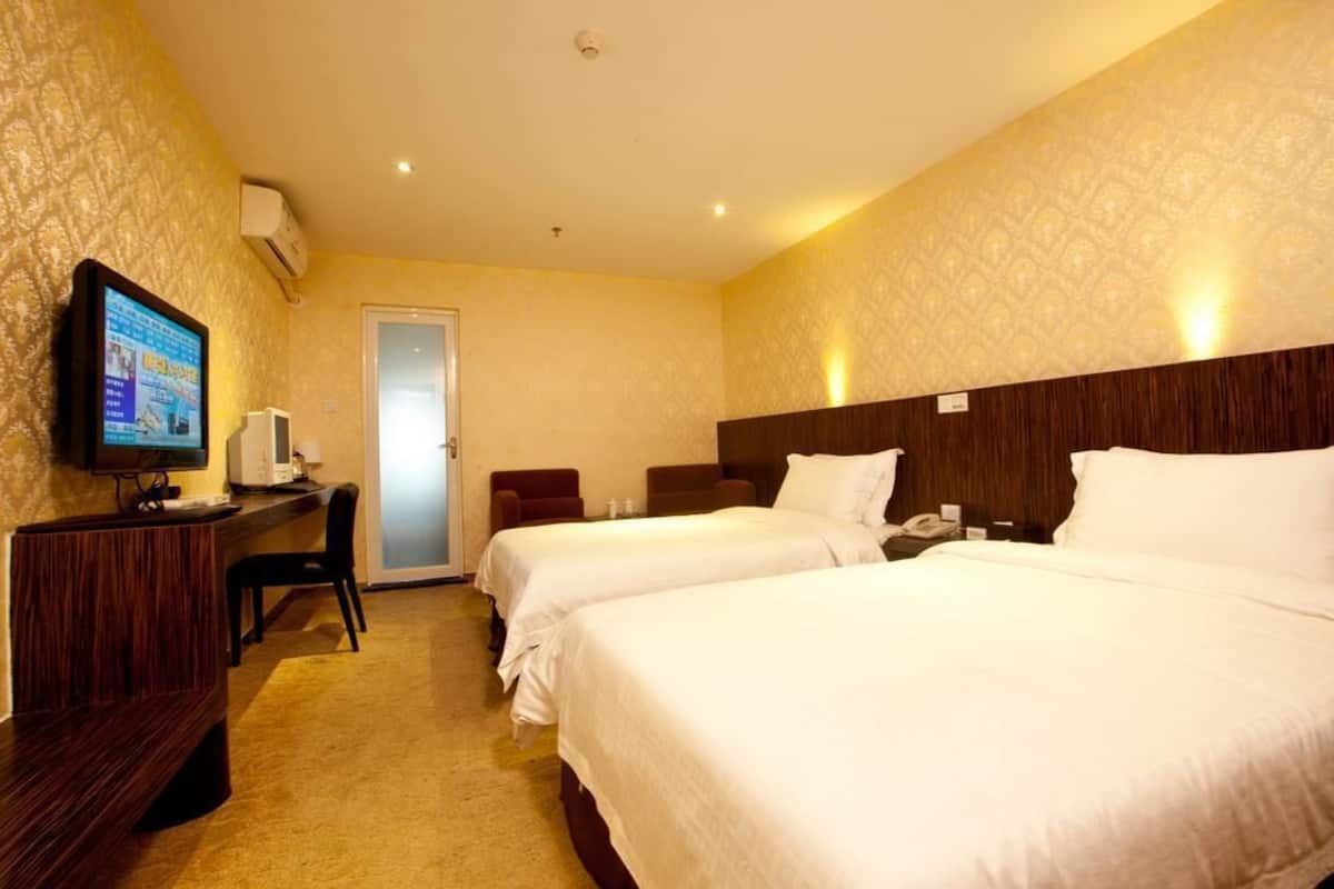 A hotel room with two beds, a desk with a computer, a television, and a door.