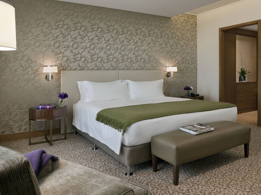 Une chambre d’hôtel avec un grand lit, deux lampes de chevet, une petite table avec un vase et un banc.