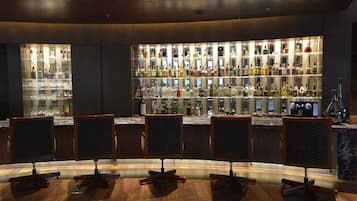 Eine Bar mit mehreren Regalen voller Spirituosenflaschen und Gläsern, Holztresen und Barhocker.