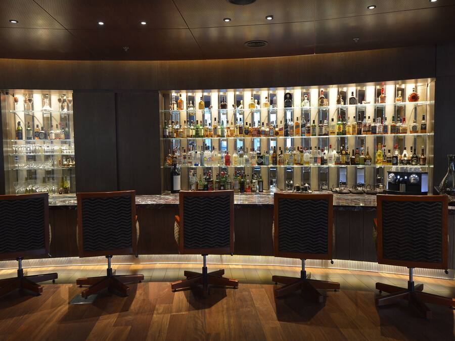 Eine Bar mit mehreren Regalen voller Spirituosenflaschen und Gläsern, Holztresen und Barhocker.