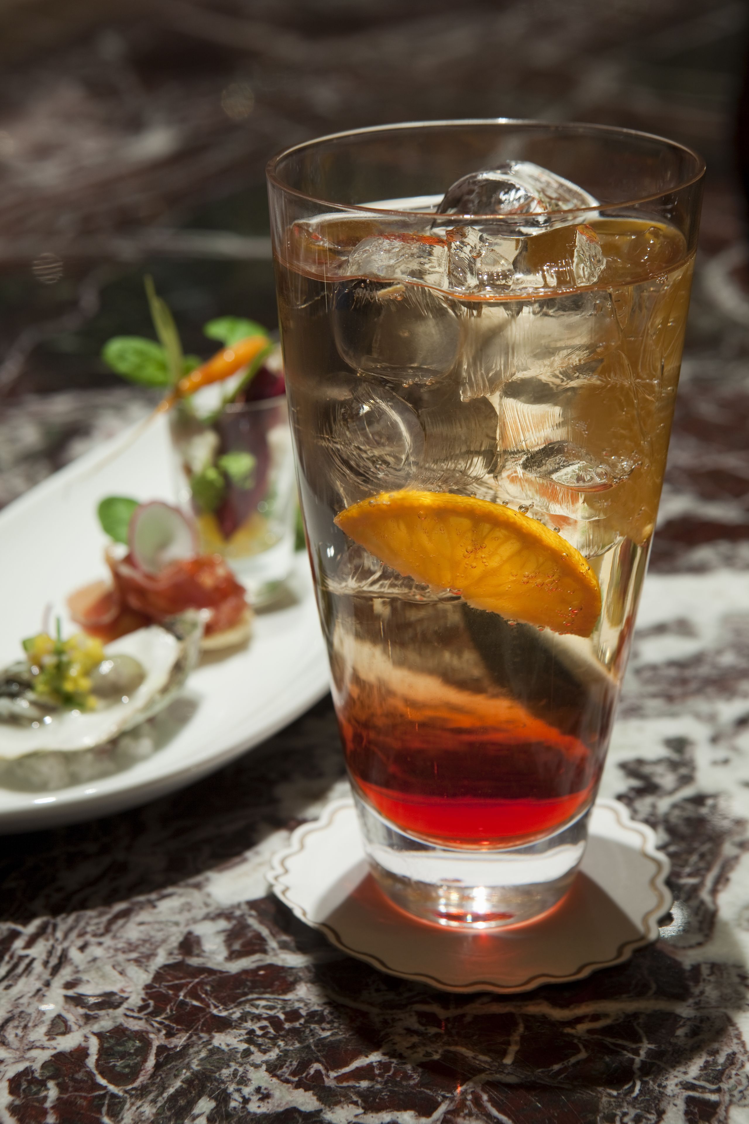 A tall glass with ice cubes and a slice of orange, placed on a marble table.