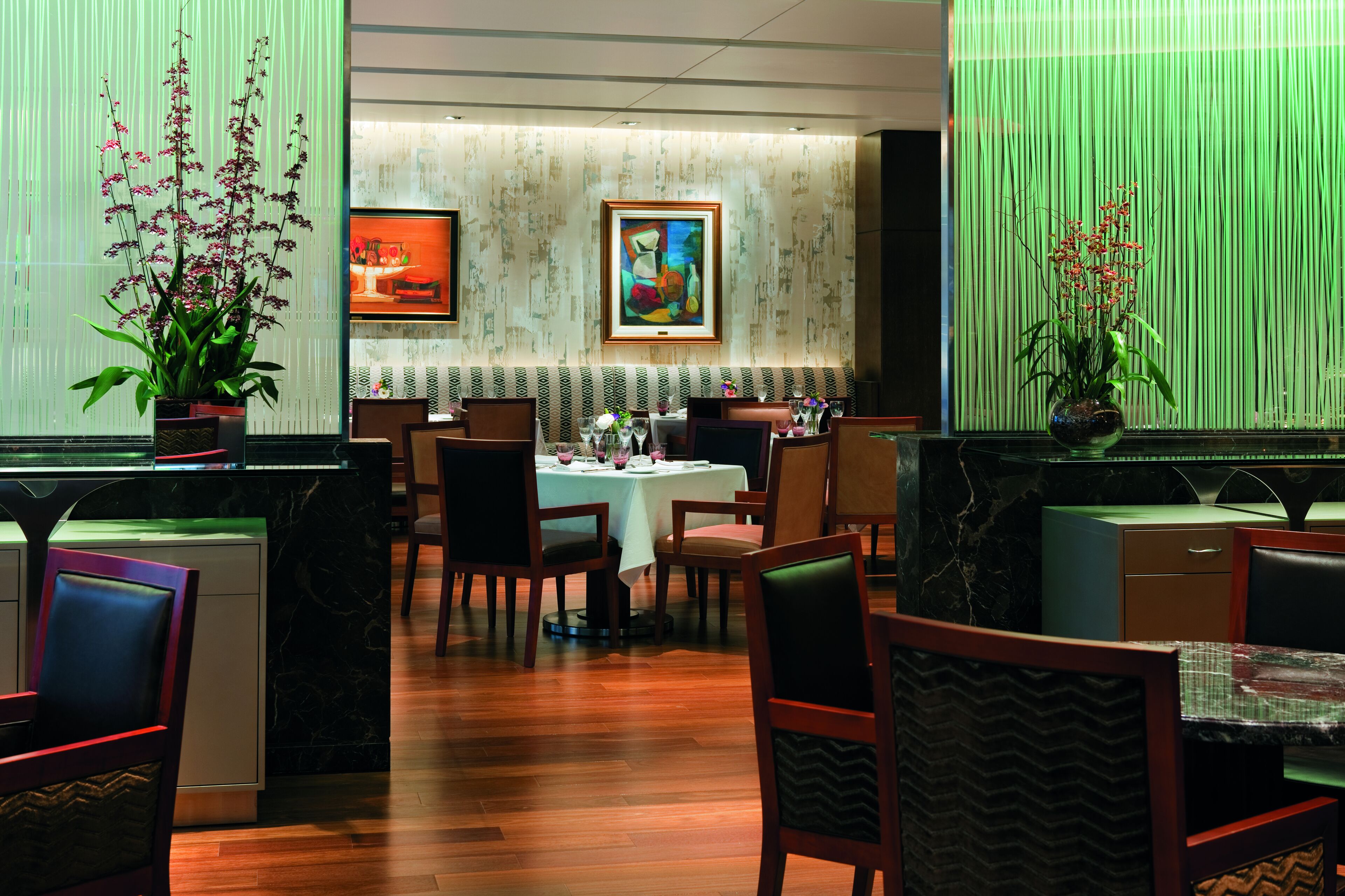 A restaurant with a marble floor, wooden chairs, a white tablecloth, and a painting on the wall.