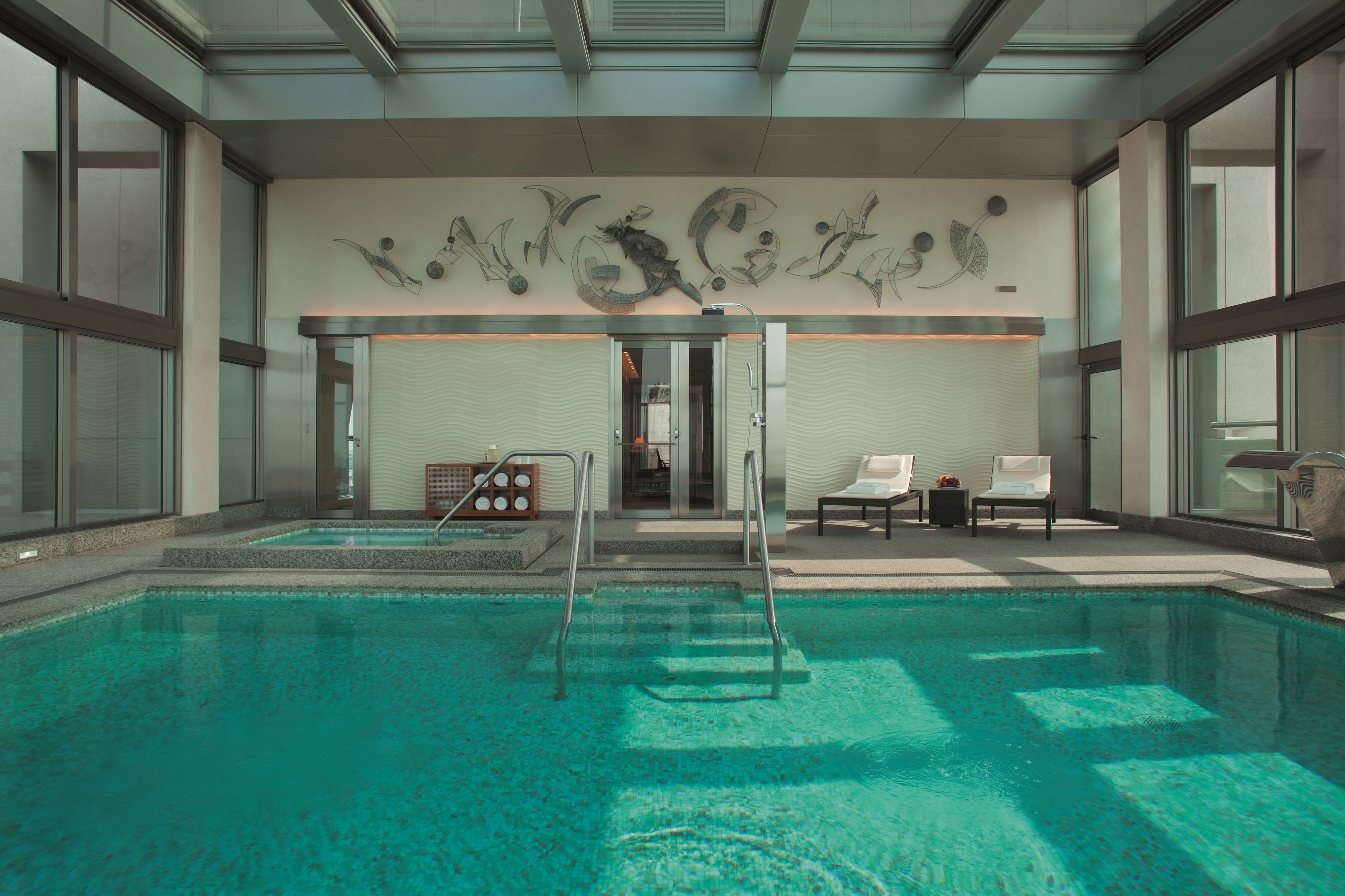 Una piscina con diseño moderno, techo de cristal e instalación artística en la pared.
