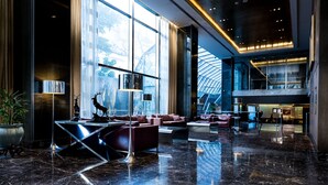 Eine großzügige Lobby mit modernem Design, ausgestattet mit einer gemütlichen Sitzecke, einer Rezeption und Blick durch große Fenster nach draußen.