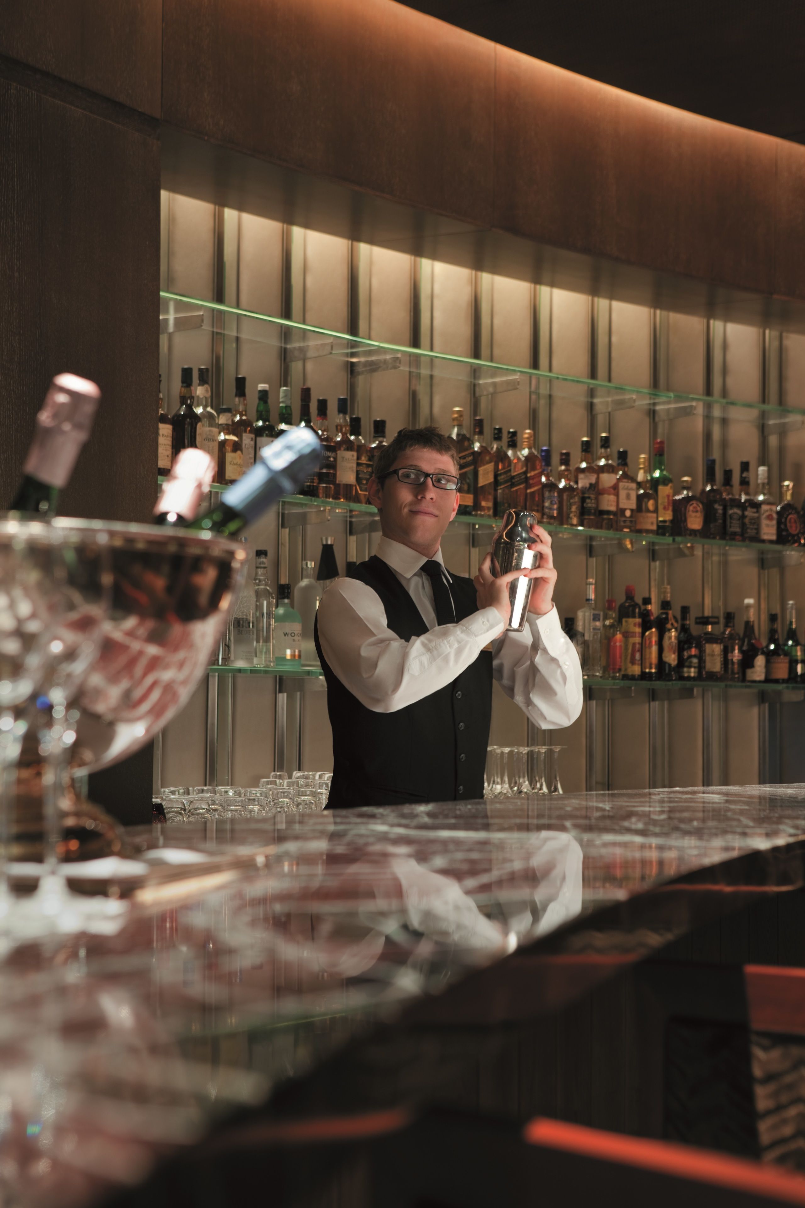 En bartender laver en drink bag baren med reoler fulde af flasker og glas.