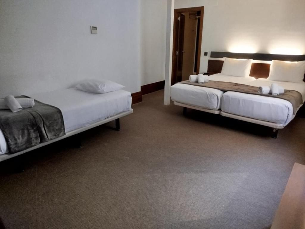 A hotel room with two single beds and one double bed, all with white linens.