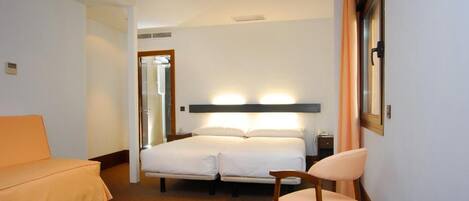 A hotel room with a bed, a chair, a desk, and a window.