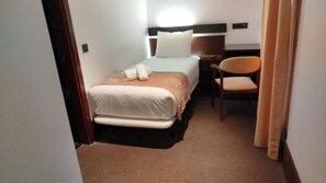 A small hotel room with a single bed, a chair, and a desk.