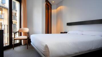 A hotel room with a bed, a chair, a nightstand, and a window with curtains.