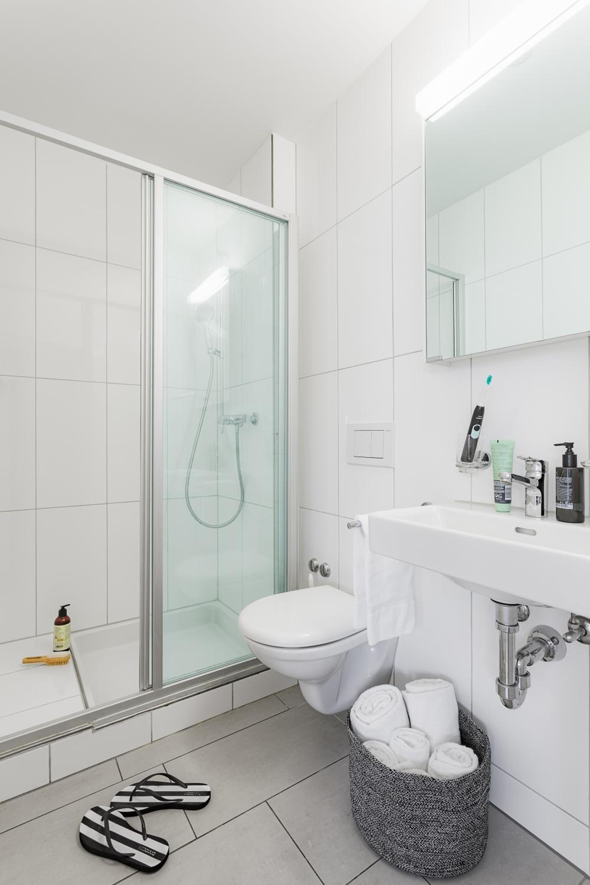 A modern bathroom with a glass shower enclosure, a white sink with toiletries, and a towel rack.