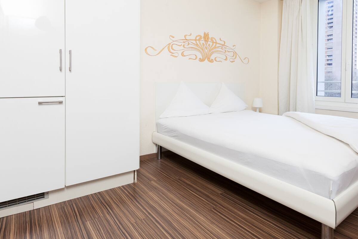 A bedroom with a bed, white wardrobe, and a decorative wall piece.