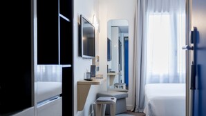 Ein Hotelzimmer mit Bett, Schreibtisch, Computer, Spiegel und einem Fenster mit Vorhängen.