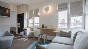 Ein modernes, helles Zimmer mit einer Couch, einem kleinen Tisch, einem Fernseher und einem Kleiderschrank.