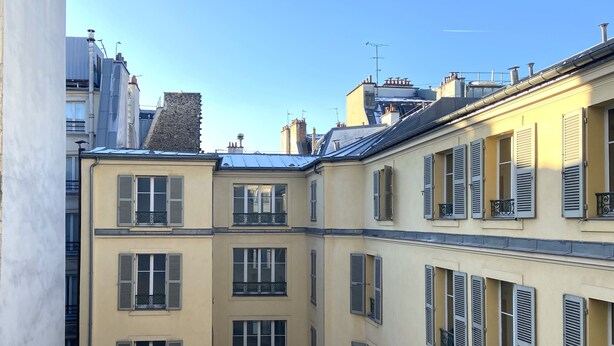 Ein mehrstöckiges Gebäude mit einem zentralen Innenhof, das Balkone und Fenster mit Fensterläden aufweist.